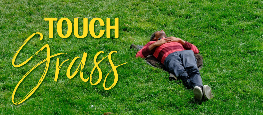 Touch Grass in text, a man laying in a field of grass